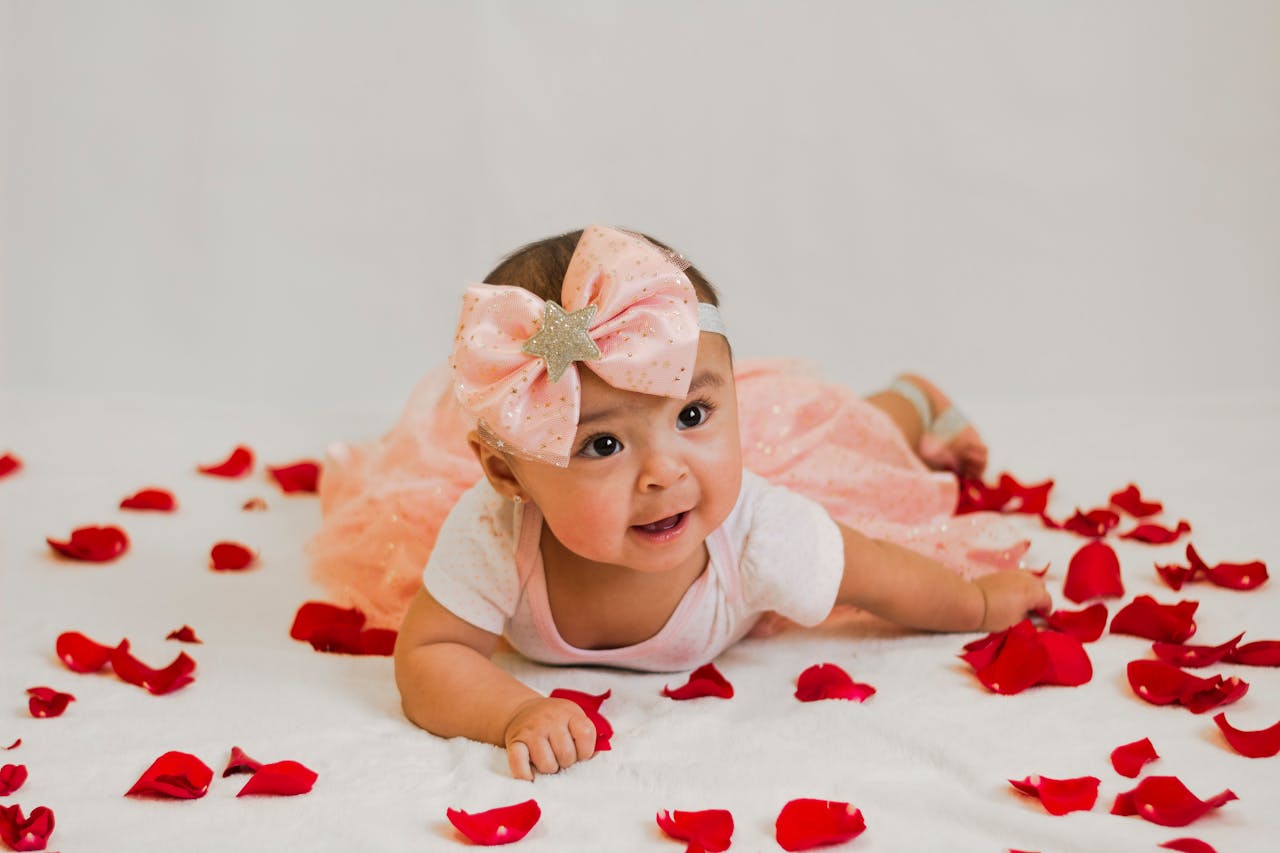 Cute baby girl laying on rose petals wearing a pink bow dress. Perfect for infant-themed photography.